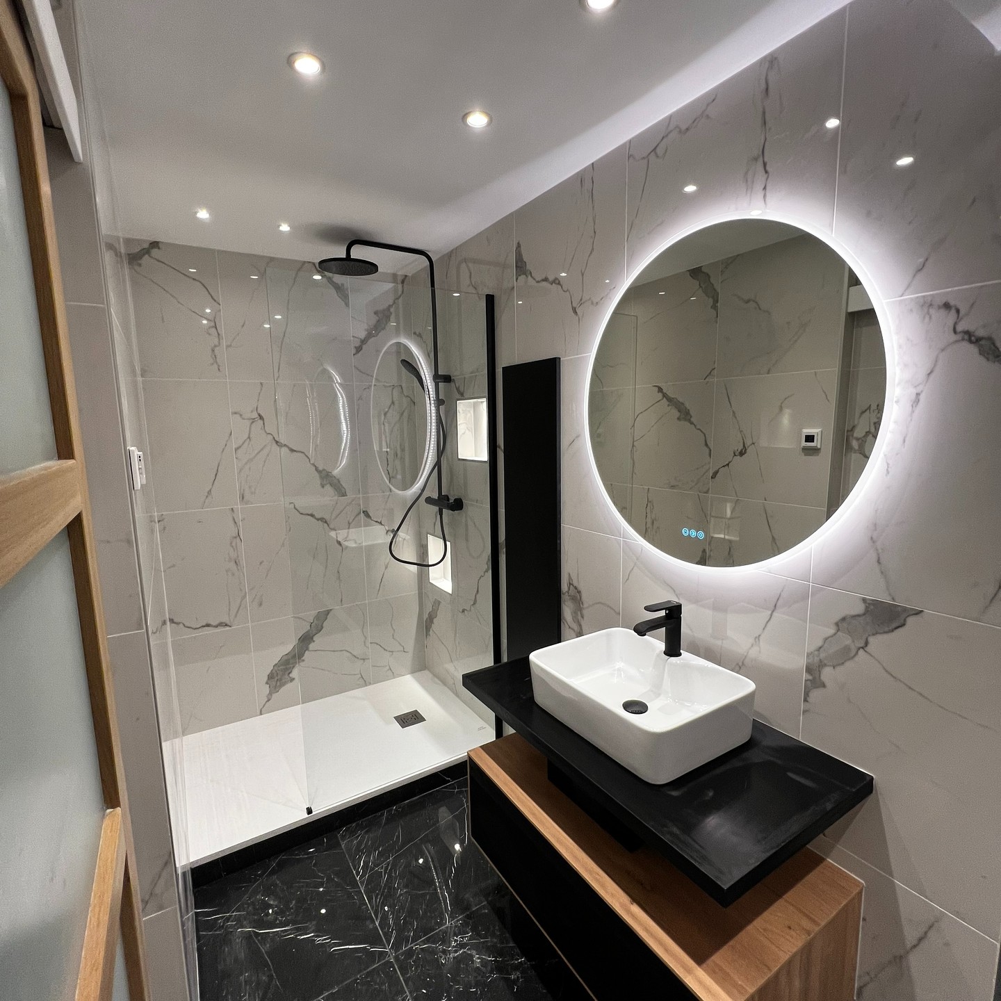 Plan de travail de cuisine avec évier rond en inox, robinet mural chromé, crédence en carreaux blancs et meubles en bois clair, éclairé par une fenêtre avec stores.